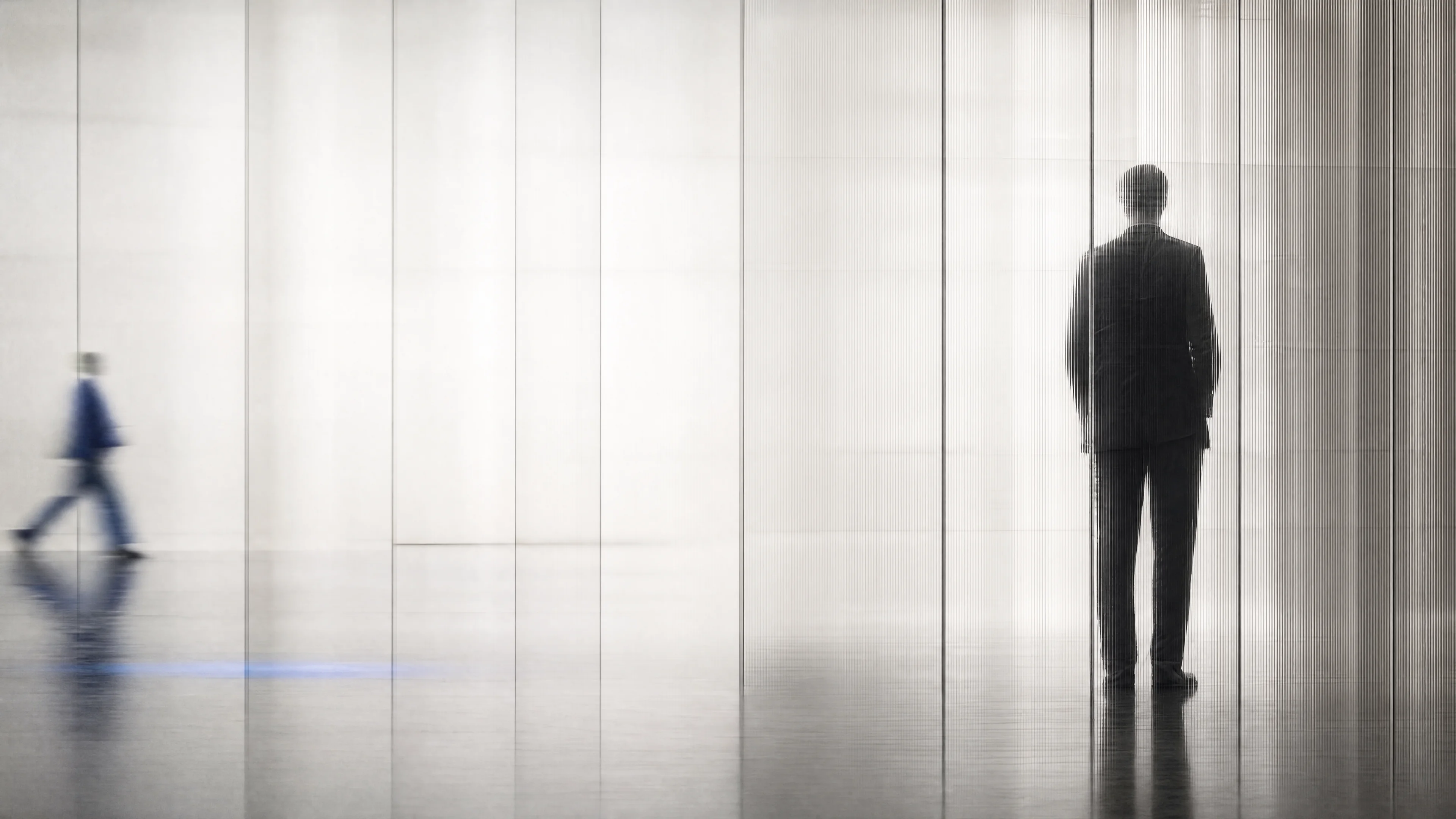 Eine ruhende Silhouette hinter geripptem Glas; links durchquert eine blaue Bewegungsfigur den hellen institutionellen Raum.